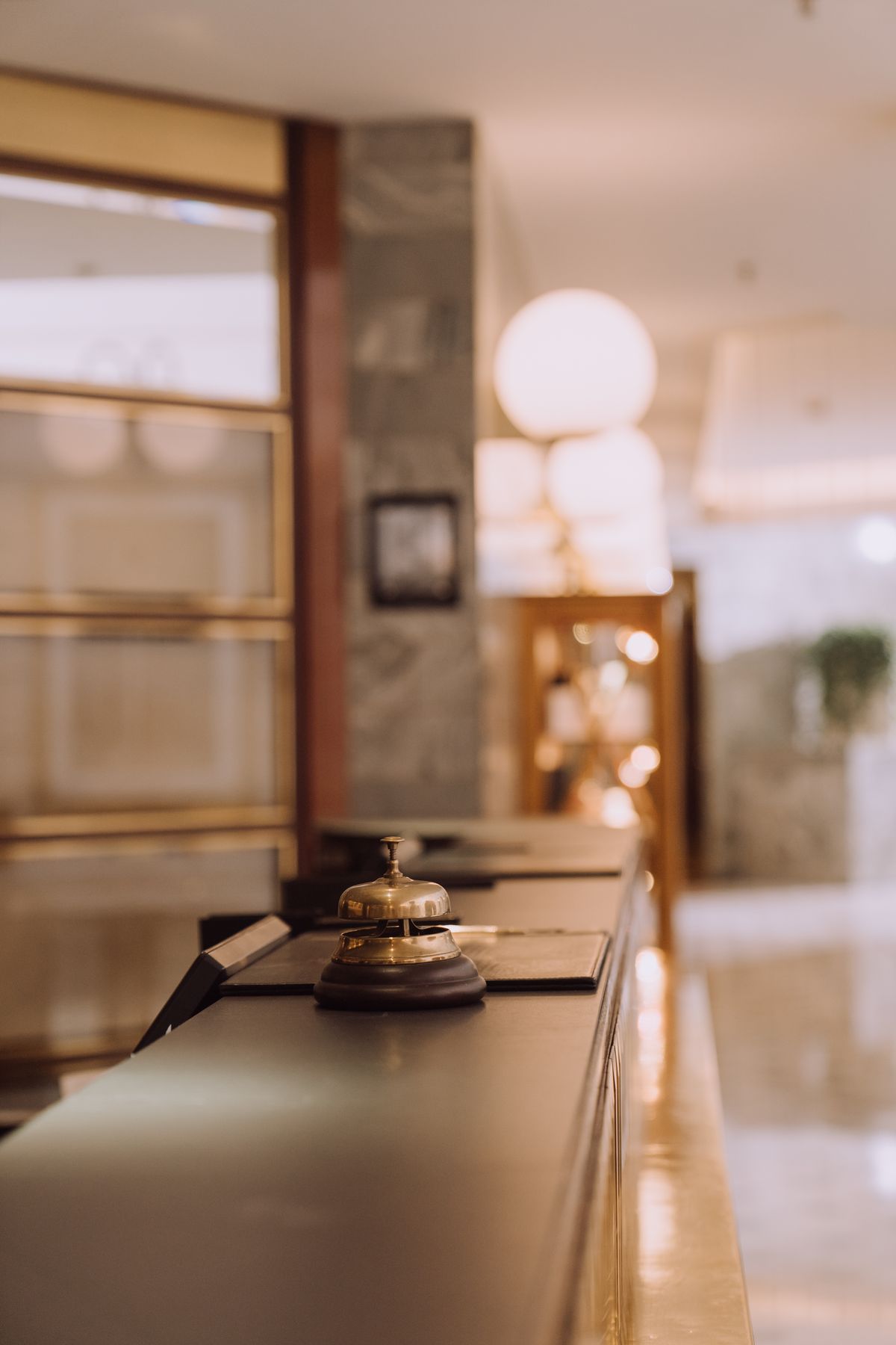 A brass bell on a long reception counter in an empty lobby.