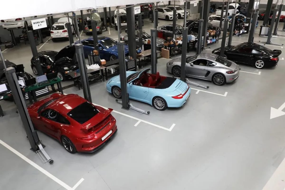 A workshop floor with two rows of red two-post lifts, cars raised on them, bonnets open.