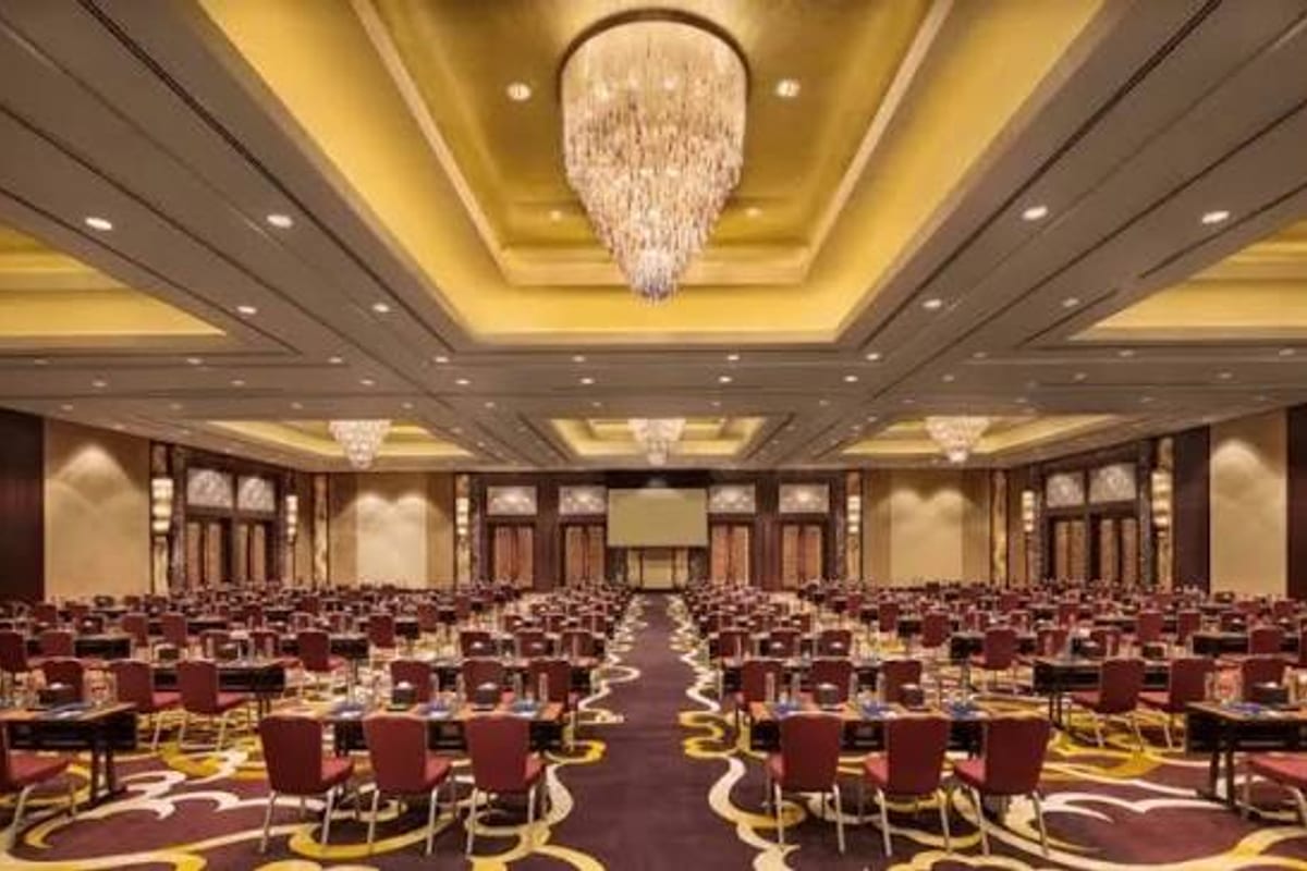 A hotel ballroom laid out for a conference: round tables, chandeliers, a screen at the far end, empty.