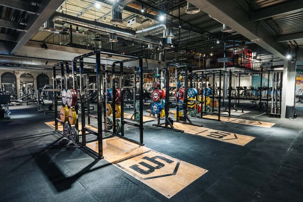 A gym floor at night: squat racks with loaded barbells, lifting platforms marked out on rubber matting.