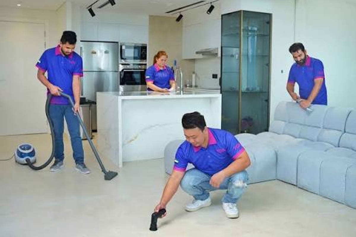 A cleaning team at work in an apartment: one vacuuming, one wiping a shelf, one working along the sofa.