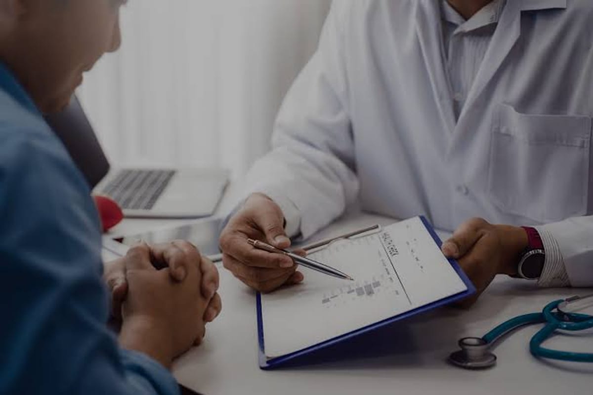 A doctor at a desk going through a chart with a patient, a stethoscope beside them.